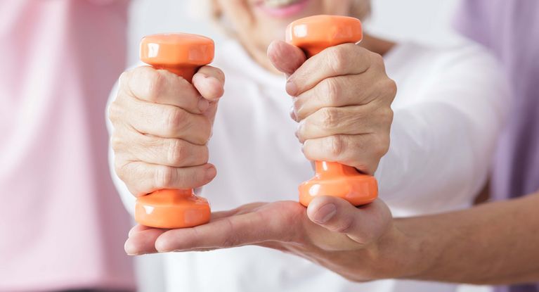 Physiotherapie in der Geriatrie Eine Seniorin trainiert mit kleinen orangefarbenen Gewichten